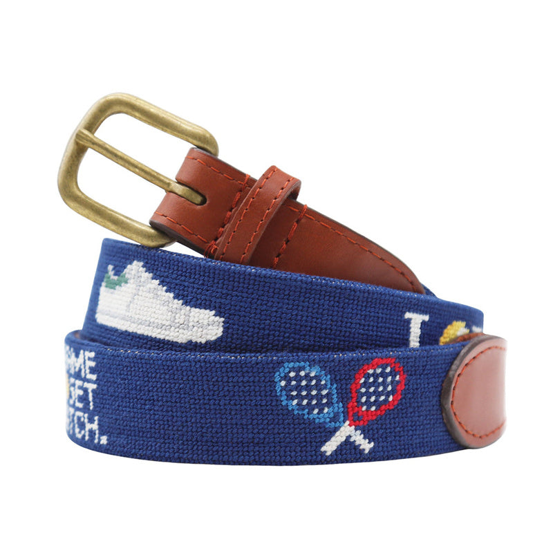 Hunting dog needlepoint belt lifestyle shot coiled on outdoor canvas bag with antique brass buckle detail