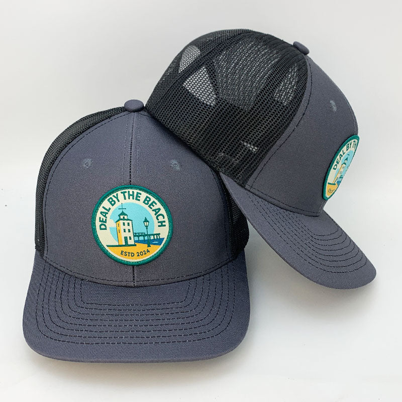 Custom charcoal black mesh trucker hat with Deal by the Beach woven patch front and back