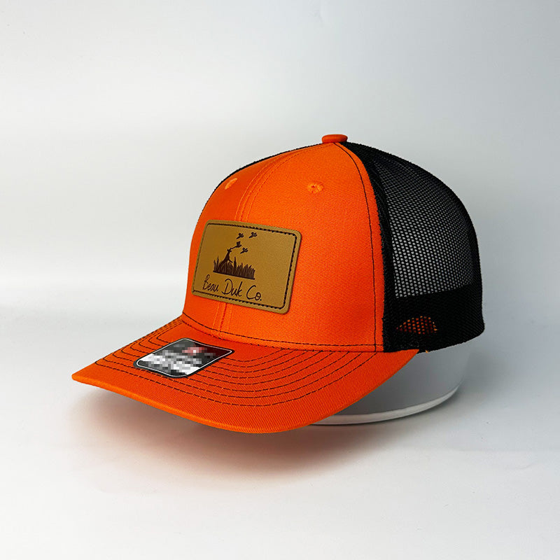 Custom blaze orange black trucker hat with Beau Duk Co laser engraved leather patch front view