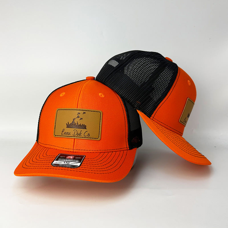 Custom blaze orange black trucker hat with leather patch angled side view