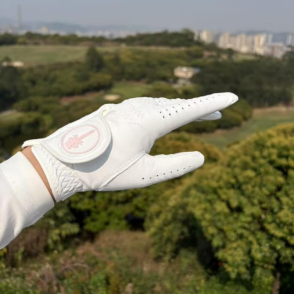 Women's cabretta leather golf glove hand raised with pink logo ball marker and golf course background